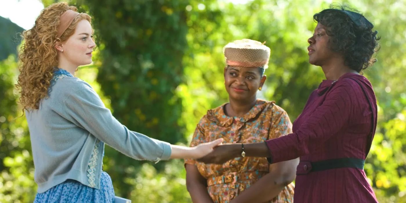 Skketer (Emma Stone) and Aibileen Clark (Viola Davis) hold hands in a sunny park while Minny Jackson (Octavia Spencer) watches on smiling 'The Help' (2011).