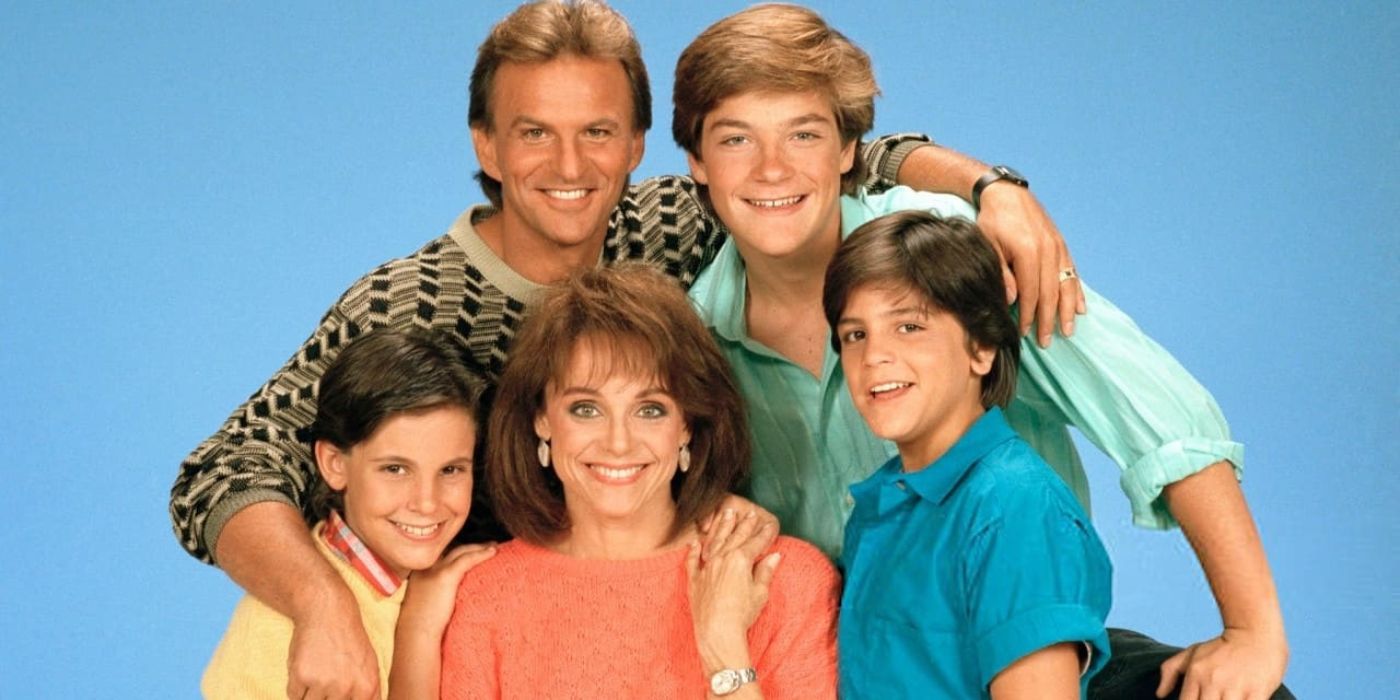 The cast of The Hogan Family pose for a traditional looking family photo with a plain blue background.