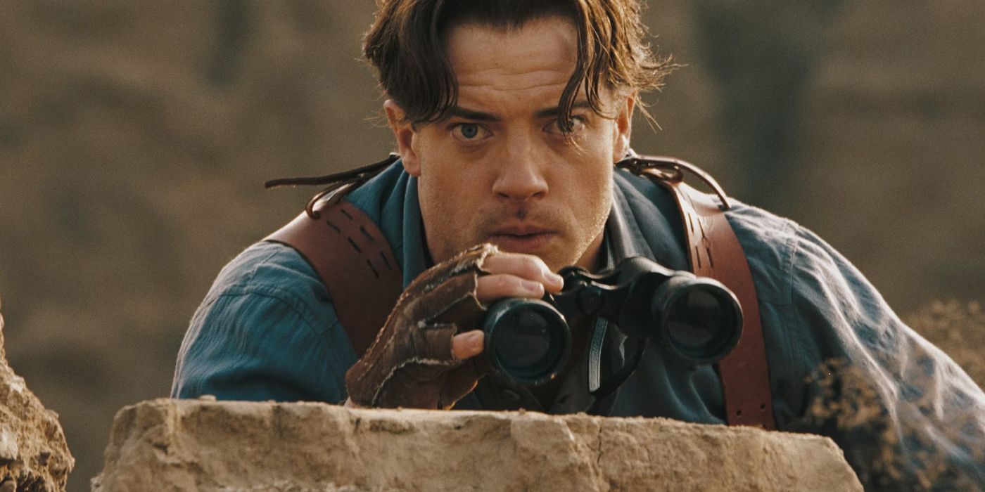 Brendan Fraser peers over a wall holding binoculars in Mummy: Tomb of the Dragon Emperor