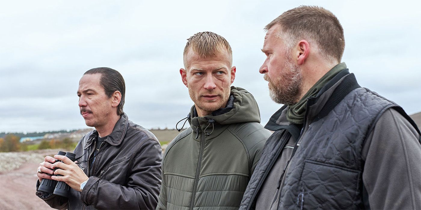 Three men standing outside, one with binoculars, two looking at each other with concern