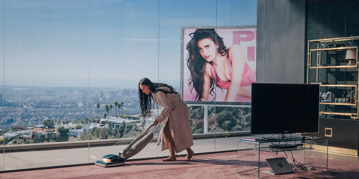 Demi Moore vacuums in front of a large window overlooking a billboard of Margaret Qualley