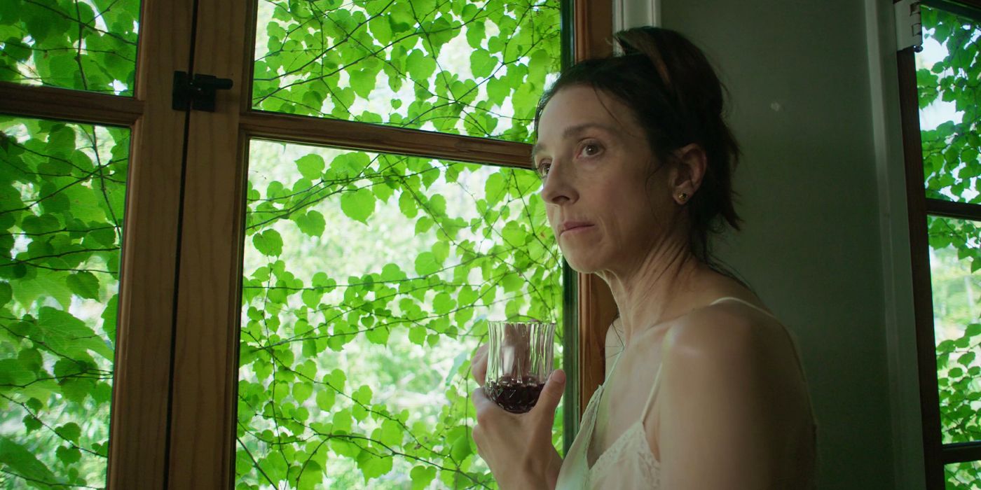 Marin Hinkle as Susanne holding a wine glass in front of a window with green vines outside