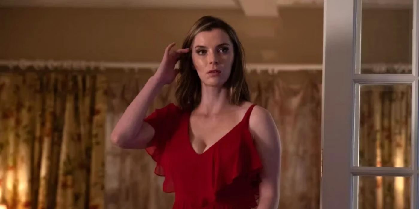 Betty Gilpin wearing a red dress and putting a strand of hair behind her ear in Three Women