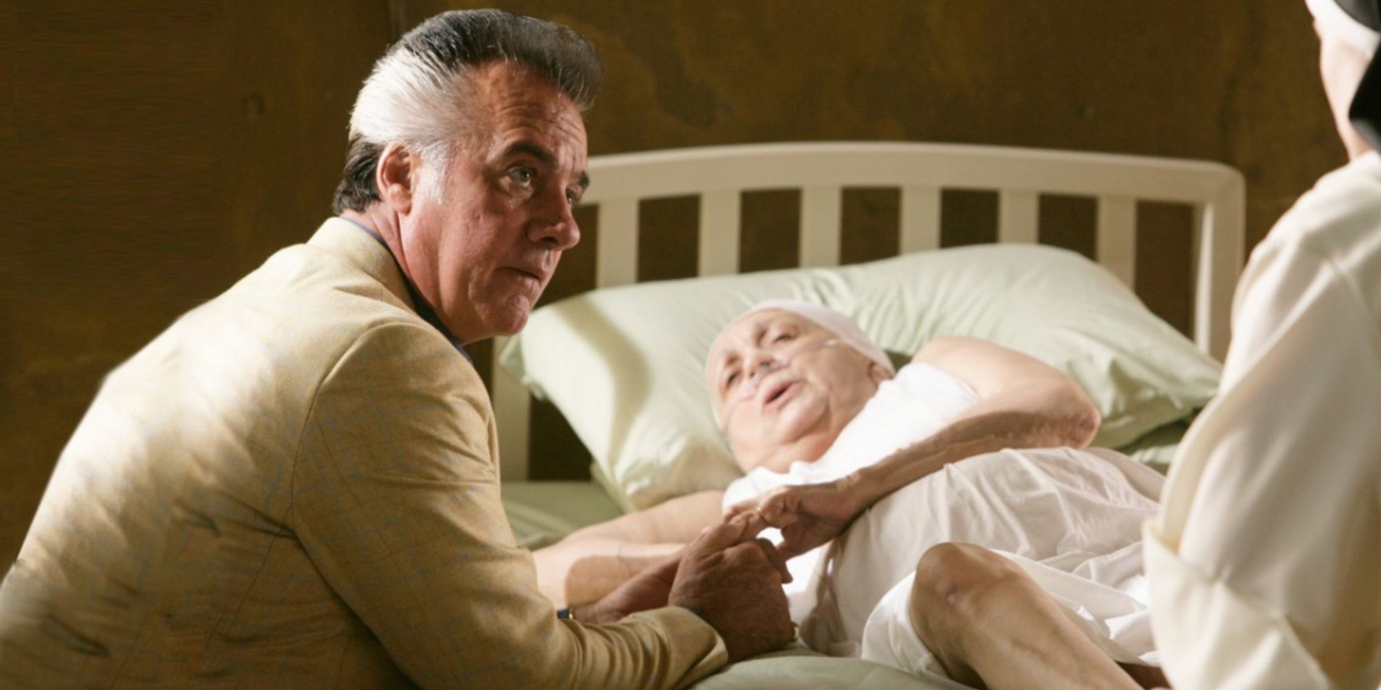 Tony Sirico sitting at Judith Malina's bedside holding her hand while looking up at someone in The Sopranos