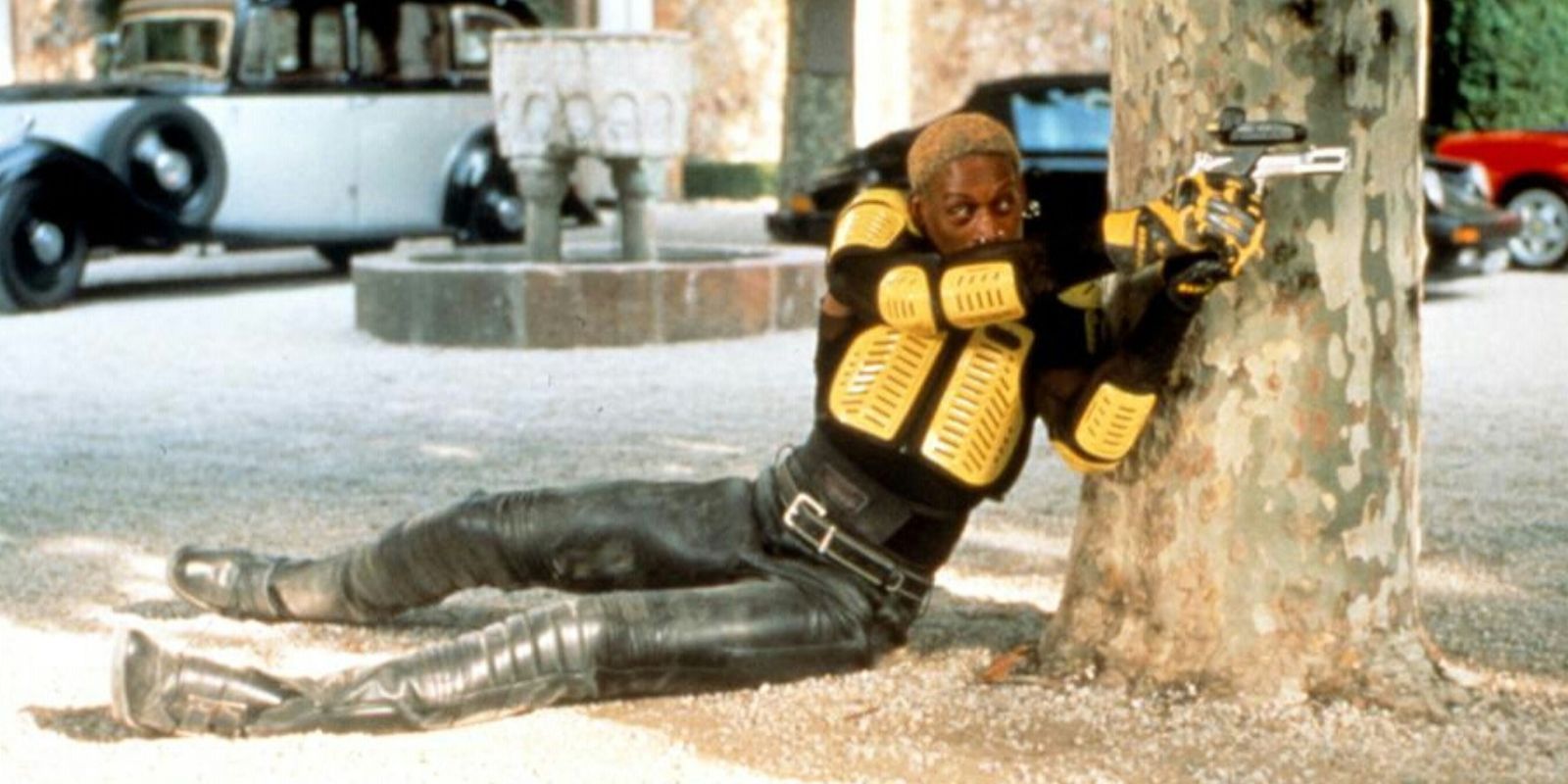 Simon laying on the ground and aiming a gun in Simon Sez