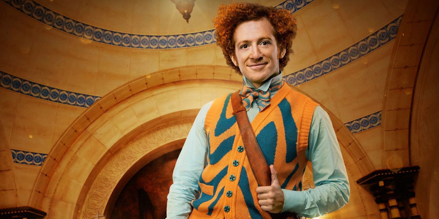 Ethan Slater as Boq wearing an orange and navy blue sweater vest and giving a thumbs up.