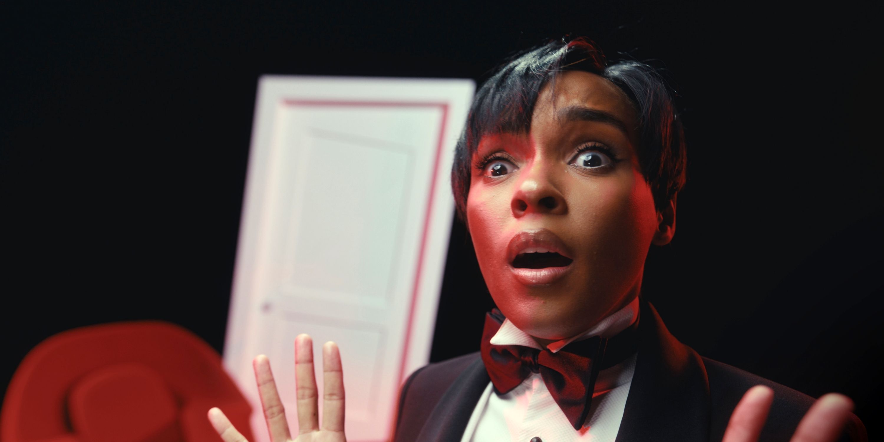 Janelle Monáe in a tuxedo holding up her hands with a shocked face as the host of AMC's FearFest