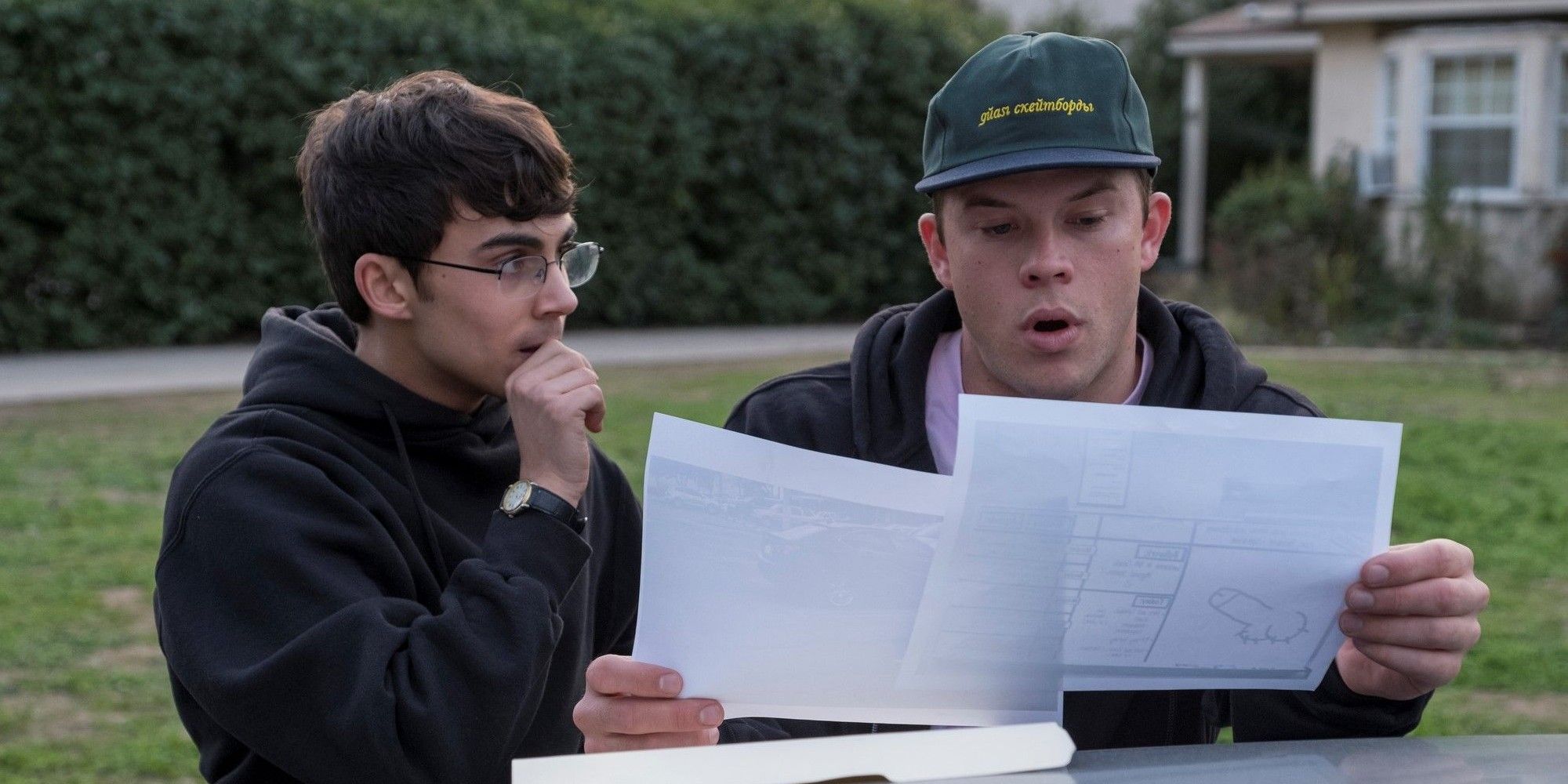 Two high school students sit at a picnic table, one showing the other paper evidence of his crimes in American Vandal