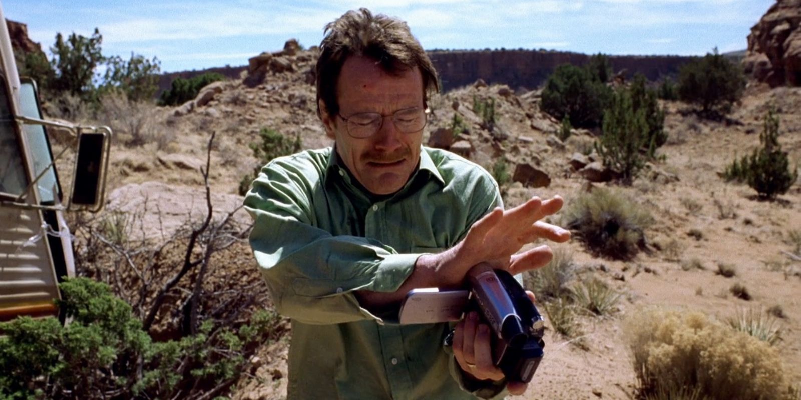 A man holds a video camera and looks desperate, standing in a desert in the Breaking Bad pilot episode.