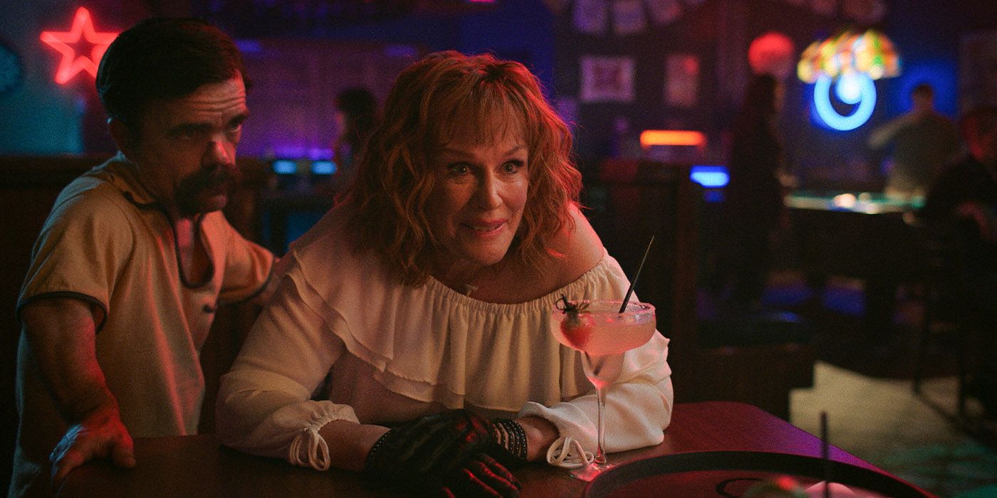 Glenn Close and Peter Dinklage at a table in a bar with a drink and gloves on