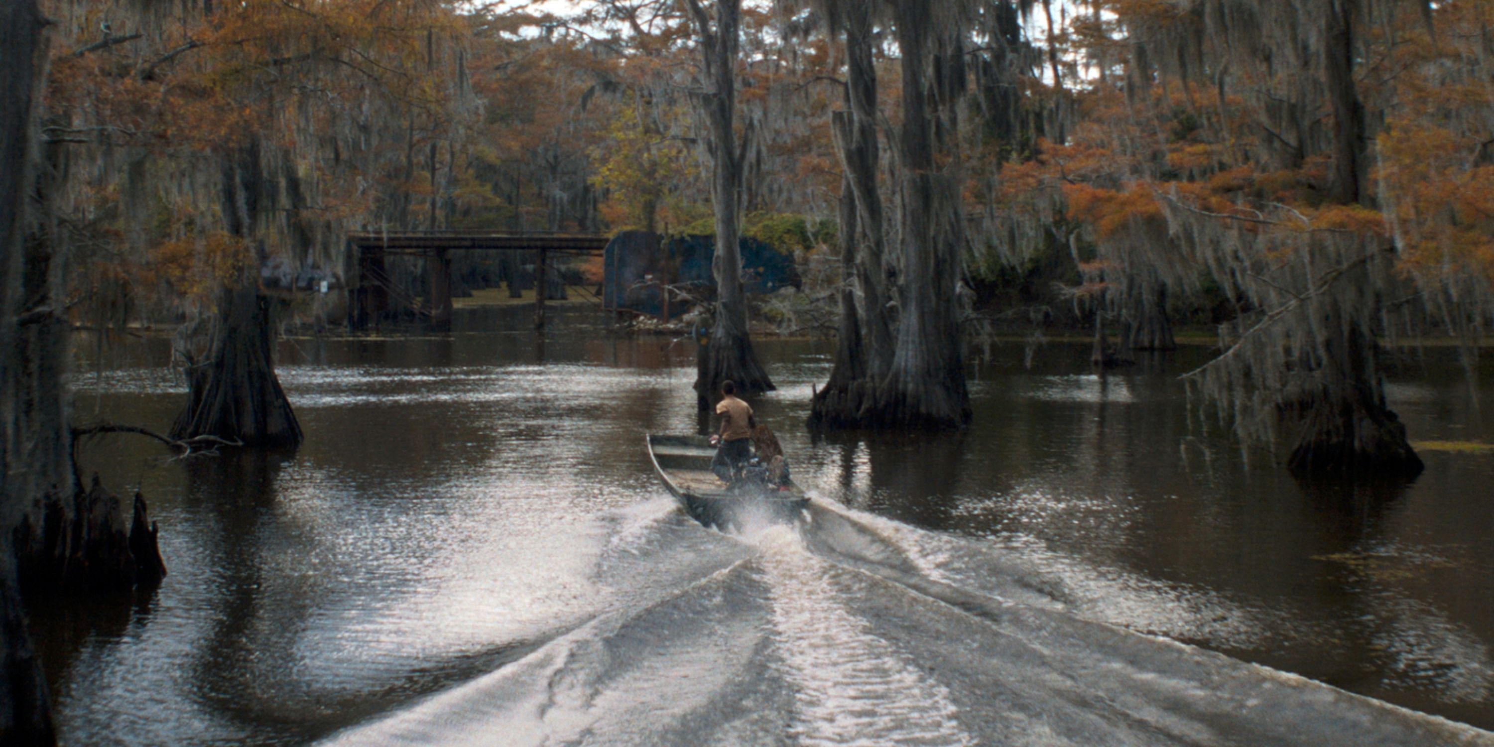 Dylan O'Brien as Paris in a boat through the trees on the lake in Caddo Lake