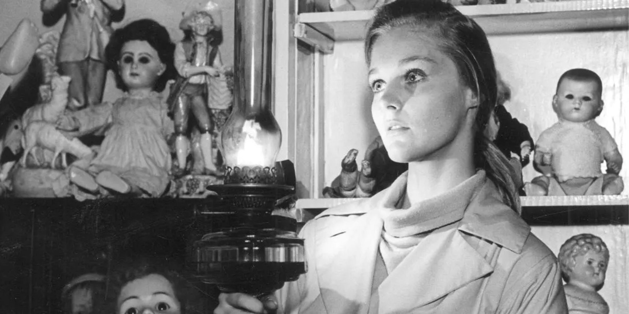 Carol Lynley as Anne Lake standing in a room surrounded by dolls holding a lit kerosene lamp in Bunny Lake is Missing (1965)
