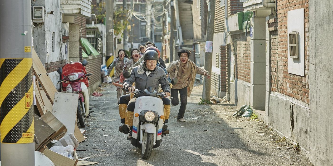 Detective Song Jae-ik in rides a moped through a narrow street as a horde of zombies chases after