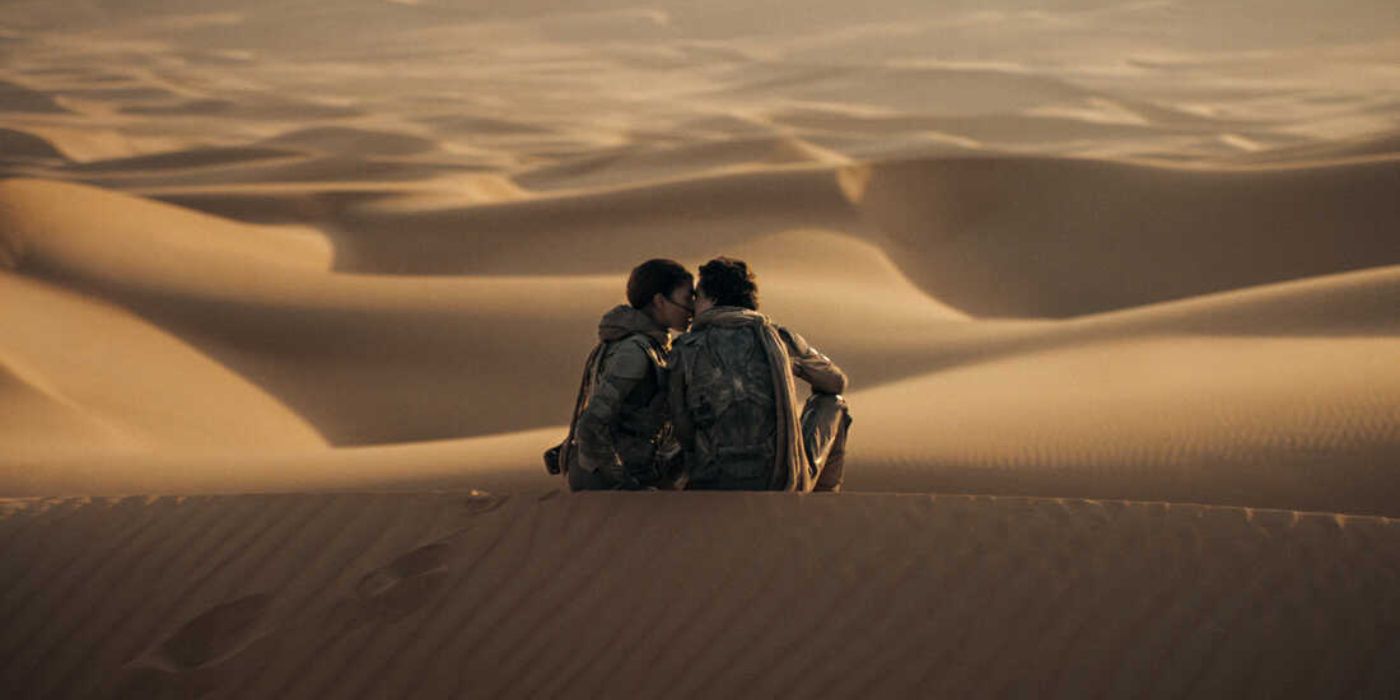 Paul Atreides (Thomthée Chalemet) and Chani (Zendaya) share a kiss as they sit atop a sand dune overlooking the vast desert landscape of Arrakis in 'Dune Part Two' (2024).