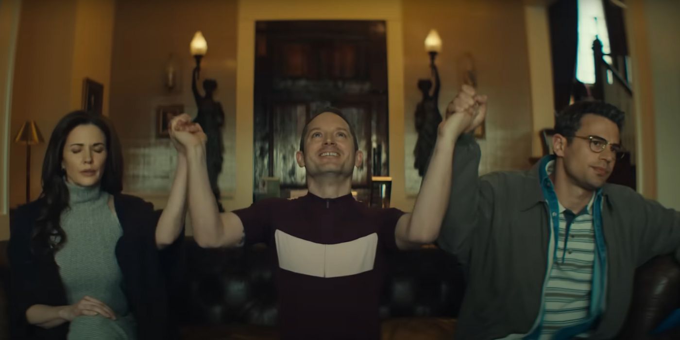 Elijah Wood and Theo James holding hands with a woman in The Monkey.