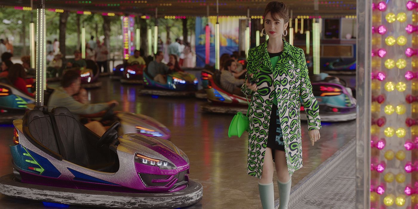 Emily from Emily in Paris walking by bumper cars in a green long jacket and high socks.