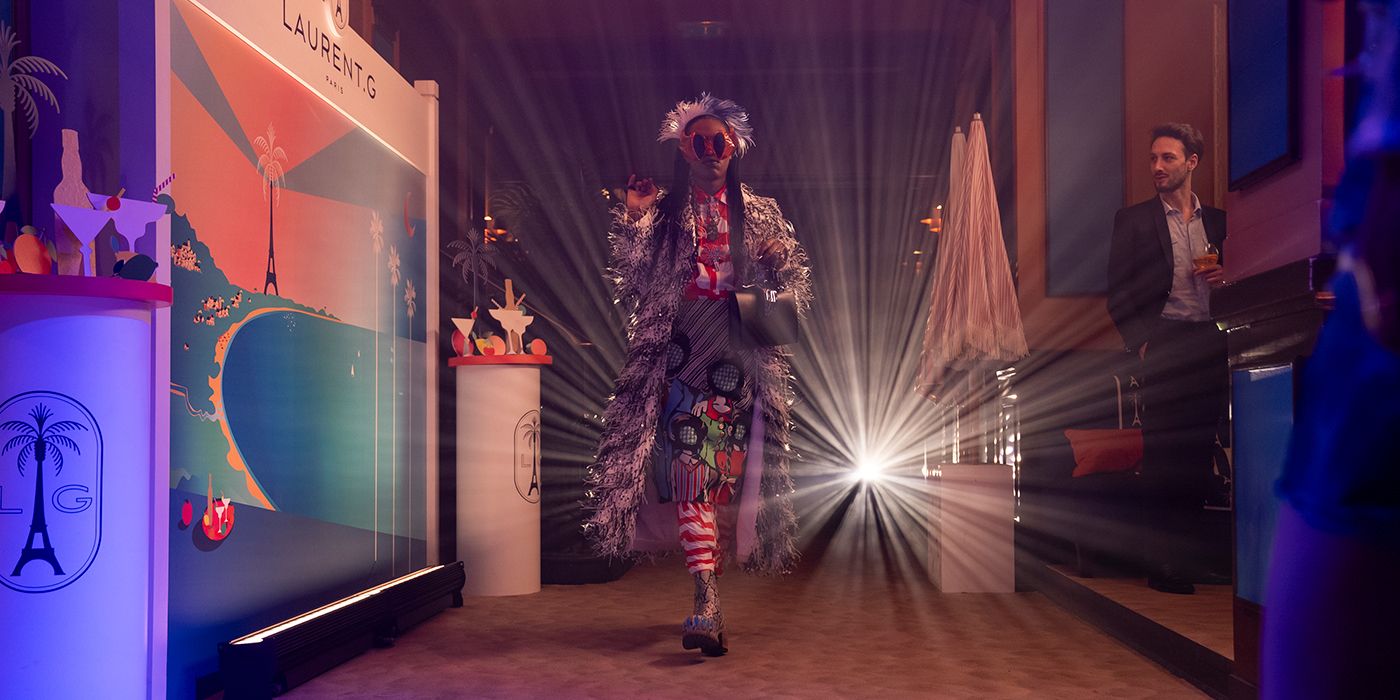 Gregory from Emily in Paris walking down a runway in an odd, mismatched outfit.