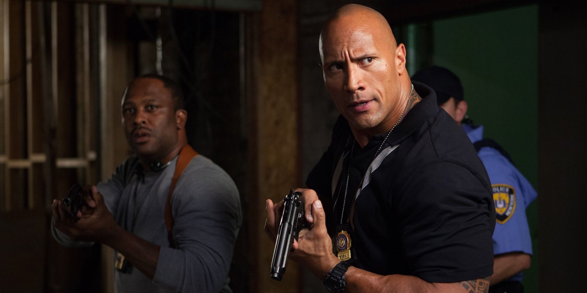 Dwayne Johnson wearing a police uniform and holding a pistol while entering a room with two other officers in 'Empire State' (2013)