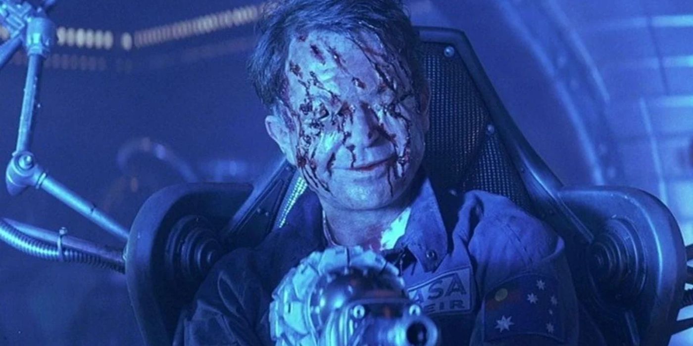 Dr. Billy Weir sits in a chair smiling with his eyes gouged out and his face covered in slices in 'Event Horizon' (1997).