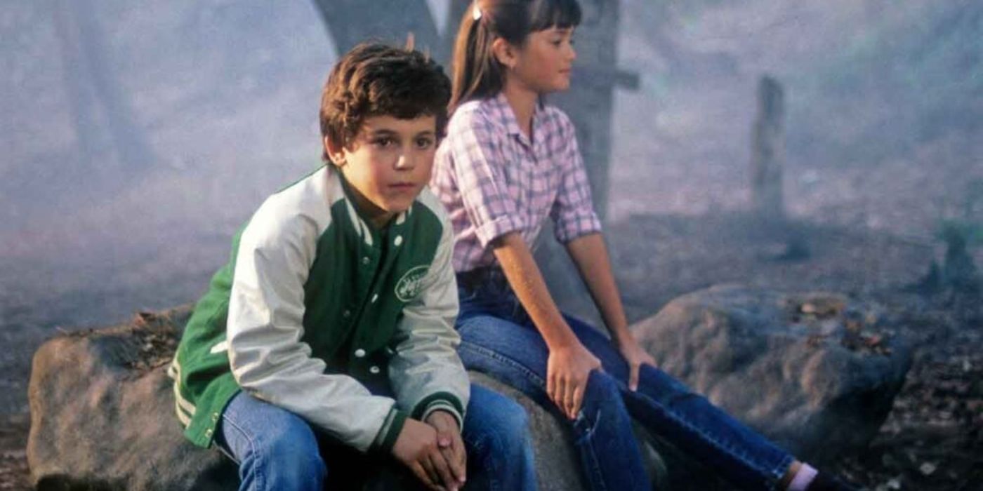 Young actors Fred Savage and Danica McKellar sit on a large rock outside on a foggy day in The Wonder Years.