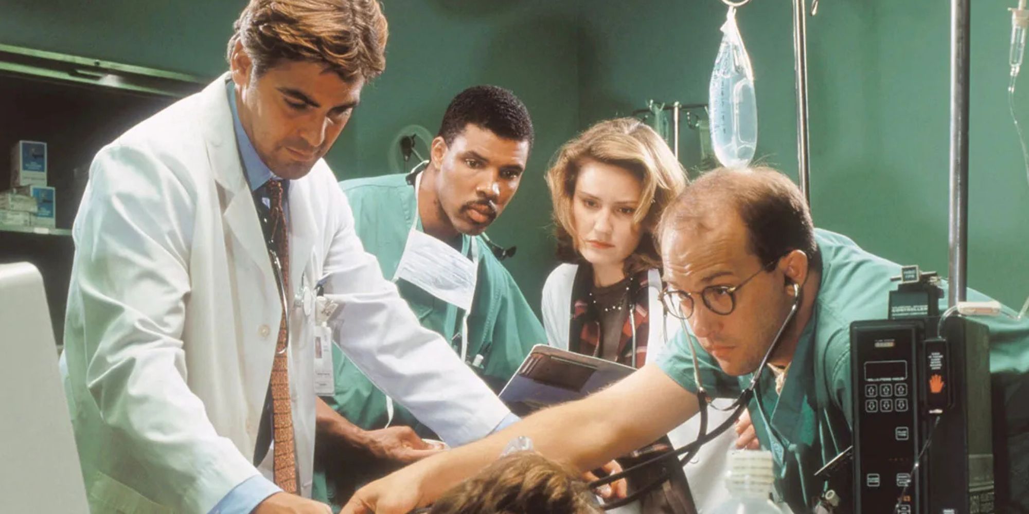 George Clooney, Eriq La Salle, Laura Innes and Anthony Edwards all standing over a patient on a hospital bed in ER