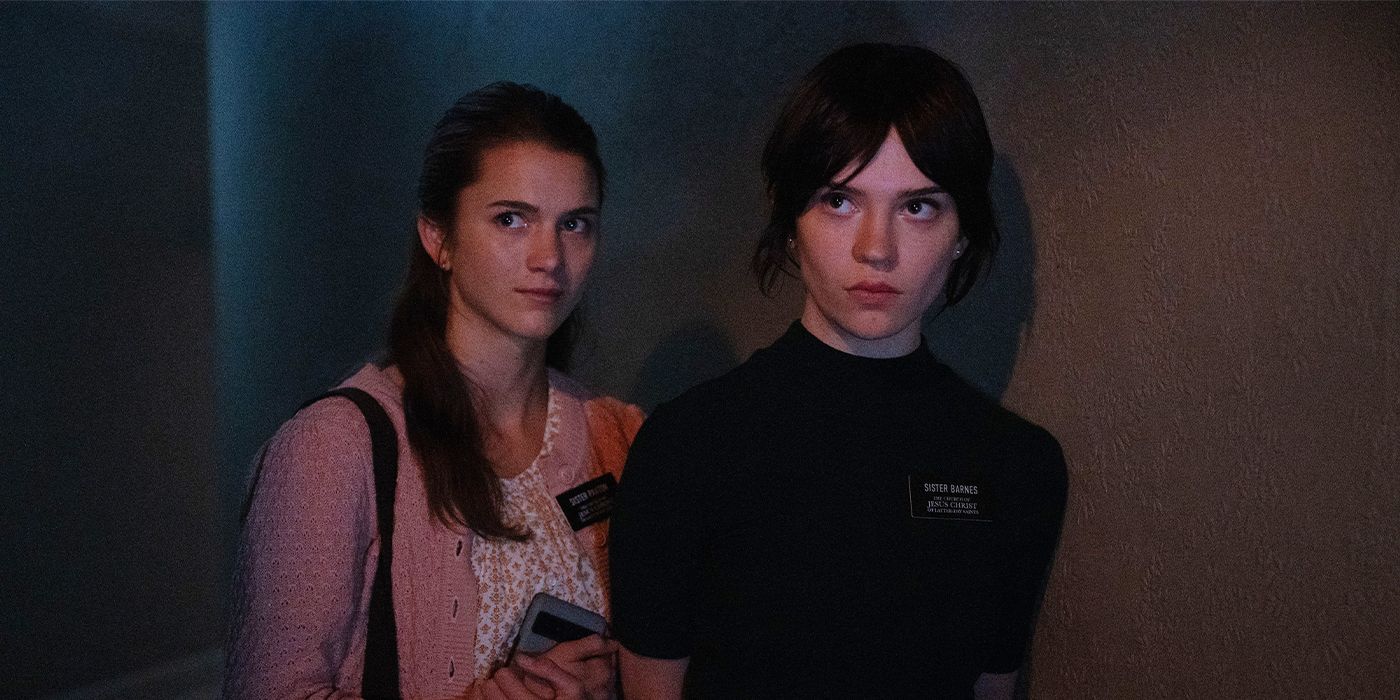 Sisters Barnes and Paxton, played by actors Chloe East and Sophie Thatcher, looking to the side fearfully in a dim room in Heretic