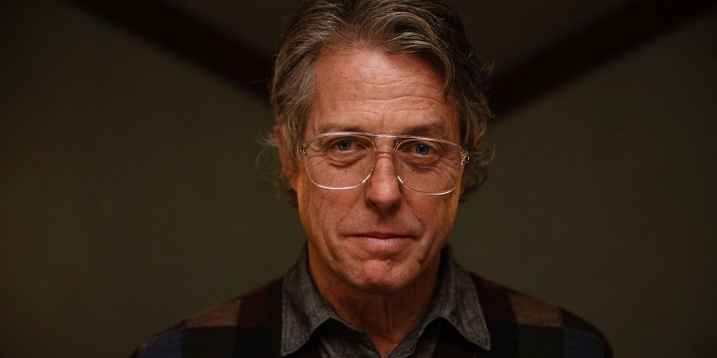 Close-up of Hugh Grant as Mr. Reed in glasses smiling down towards the camera eerily in Heretic