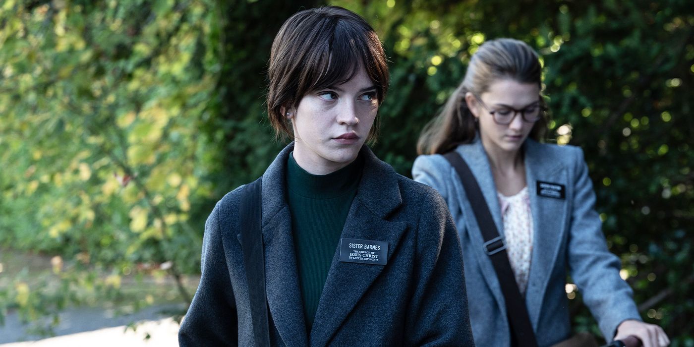 Sister Barnes, played by actor Sophie Thatcher, looks to the side ominously with Sister Paxton, played by actor Chloe East, towing a bike behind her in Heretic.