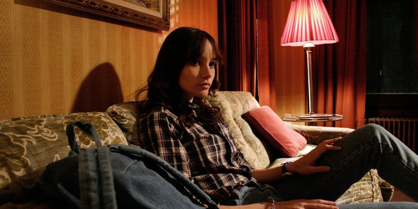 Samantha sits on a couch next to her backpack in Ti West's horror The House of the Devil.