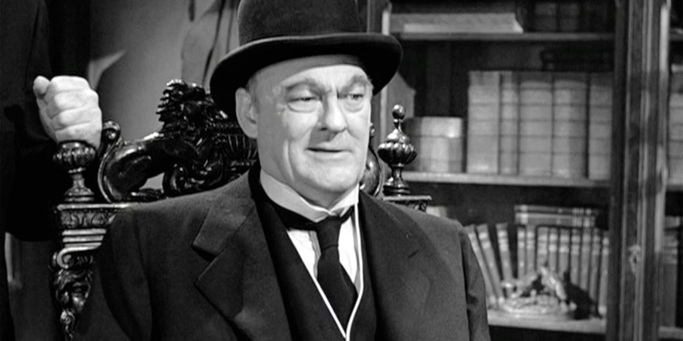 Mr. Potter (Lionel Barrymore) sits scowling and grump behind his desk as he wears a suit and a bowler hat in 'It's a Wonderful Life' (1946).