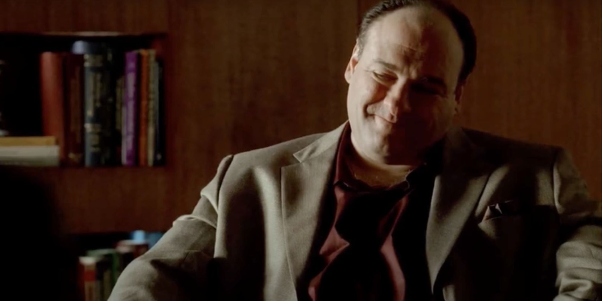 James Gandolfini as Tony Soprano sitting in a chair grinning in The Sopranos episode The Ride