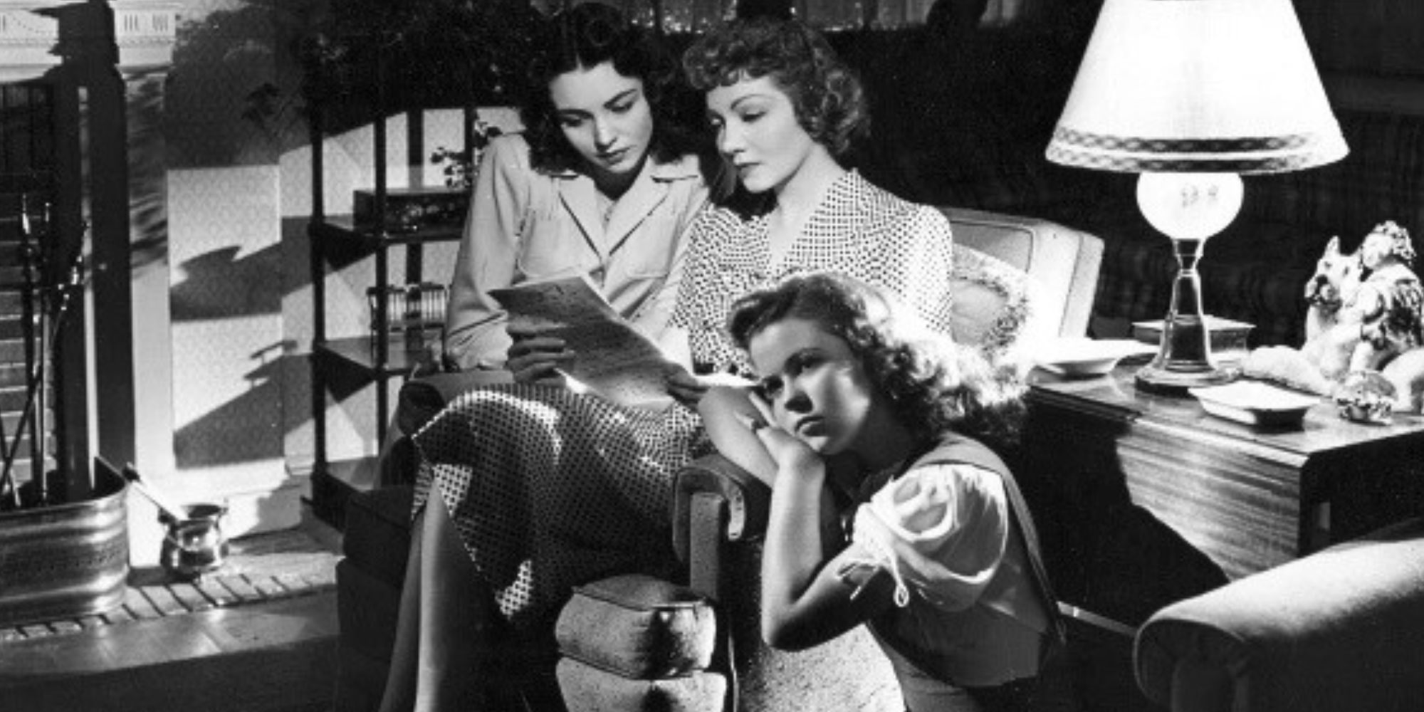 Jennifer Jones sitting with Claudette Colbert in a chair looking at a book while Shirley Temple sits on the floor resting her head on the arm of the chair in Since You Went Away (1944)