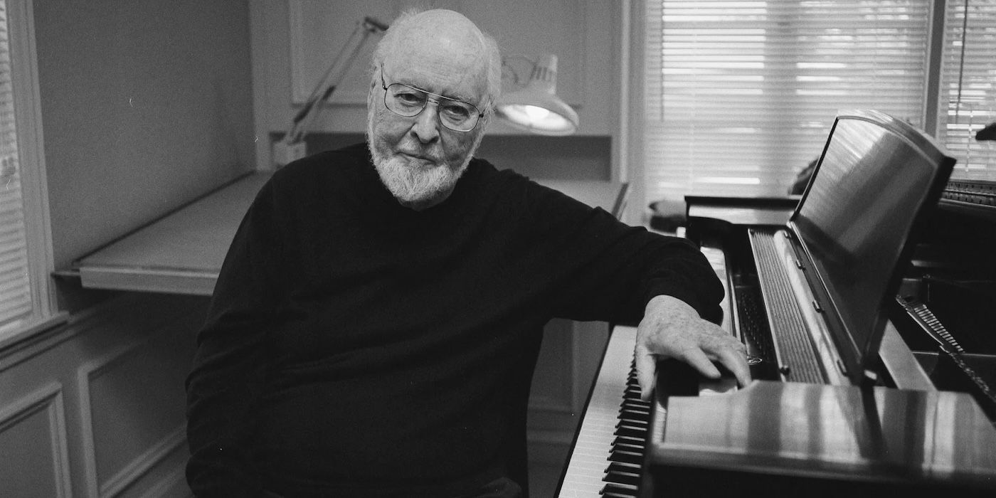 John Williams leaning his left arm on a piano above the keys in Music by John Williams