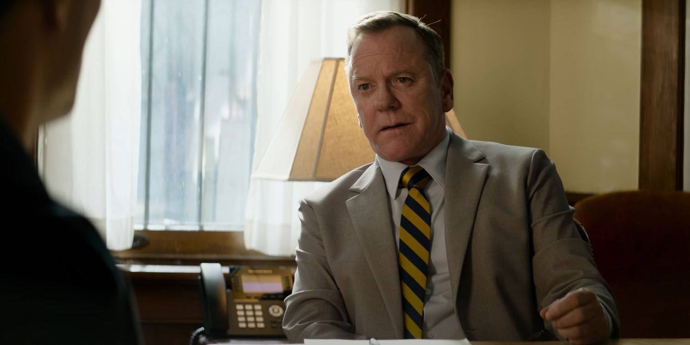 Kiefer Sutherland sitting in an office wearing a yellow and navy blue stripped tie in Juror No. 2.