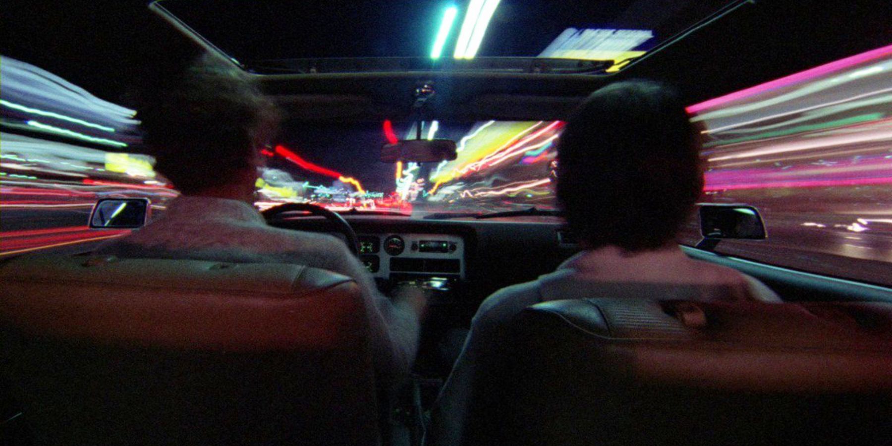 Two people in a car as the lights out the windows blur in Koyaanisqatsi