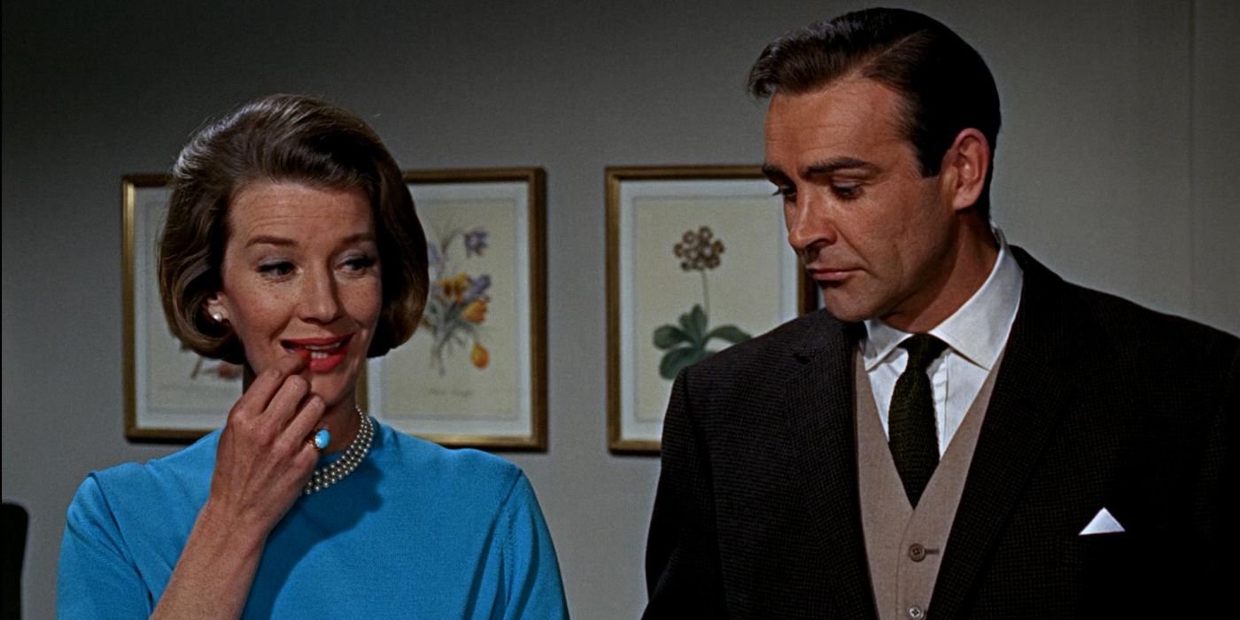 Lois Maxwell and Sean Connery standing in a room, both looking at something different off-screen in a scene from 1964's 'Goldfinger'