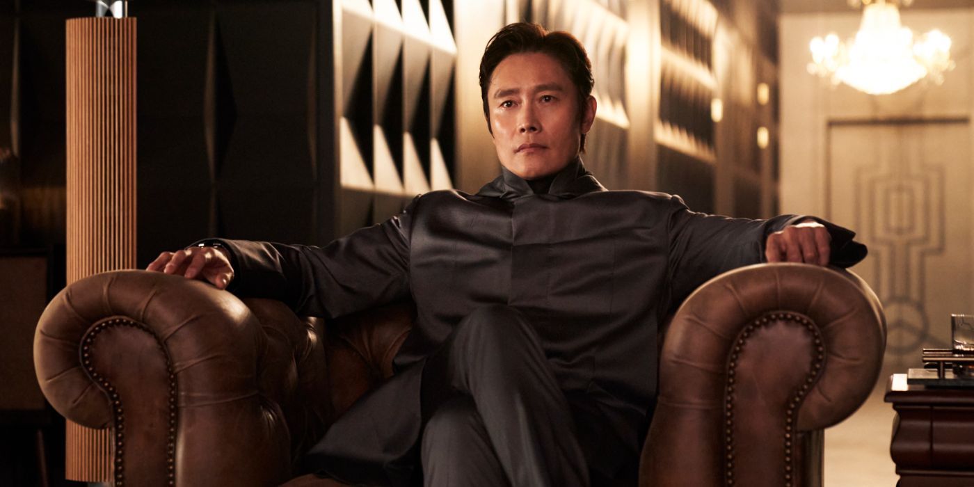 Squid Game's Front Man (Lee Byung-hun) wears all black and sits in a leather chair