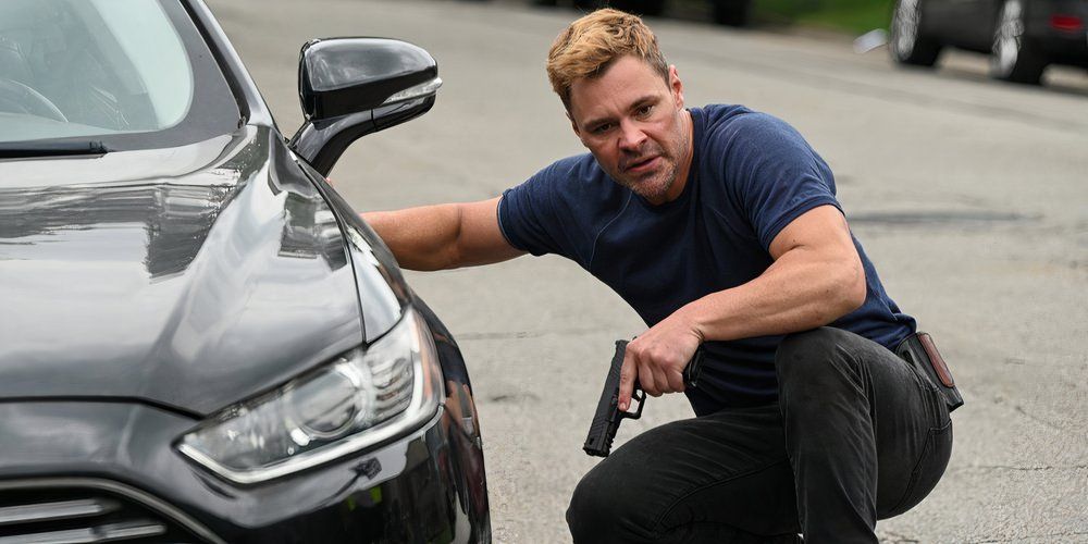 Patrick John Flueger holding a gun behind a black vehicle in Chicago P.D. Season 12 Episode 2
