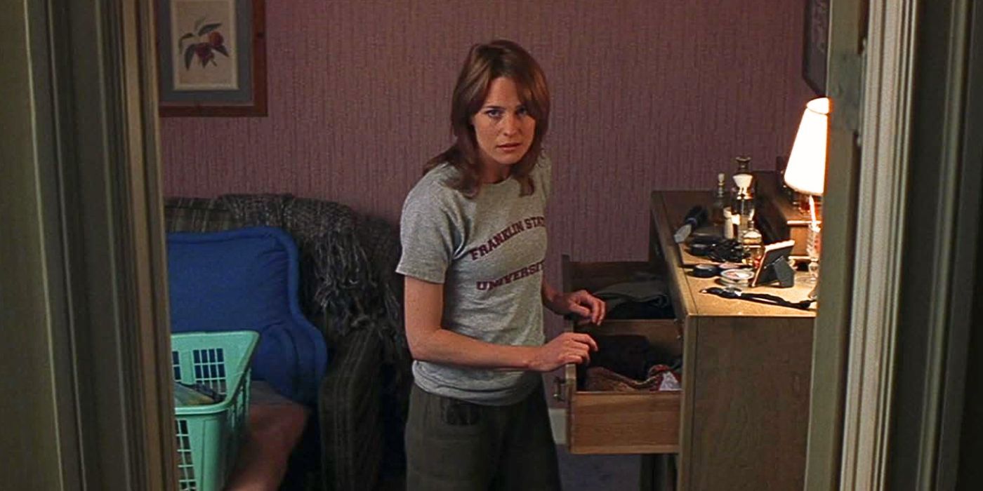 Robin Wright stands in front of an opened drawer with her hands resting on it while wearing a grey t-shirt with red lettering and looking upwards to an unknown presence off-camera from the movie Unbreakable