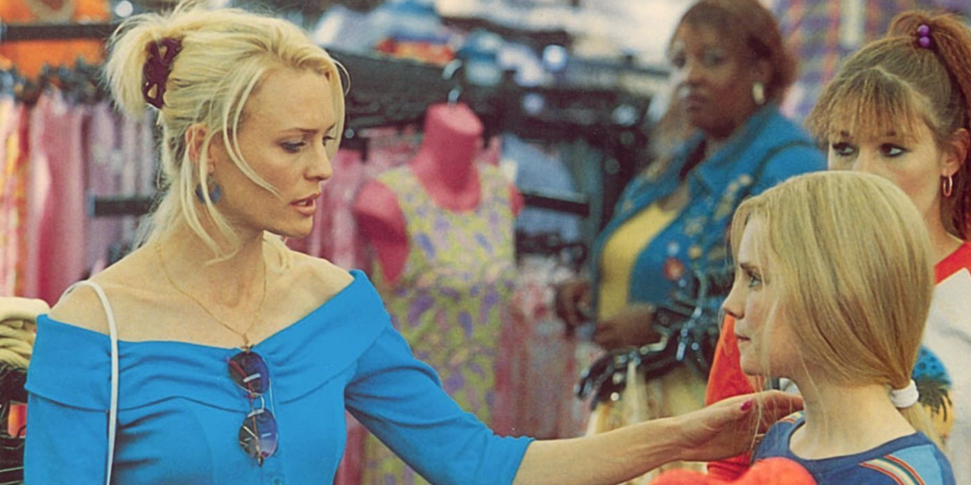 Robin Wright, wearing an off-the-shoulder blue blouse and an updo hairstyle, stands opposite Alison Lohman in a clothing store with Robin's hand resting on the young girl's shoulder from the movie White Oleander.