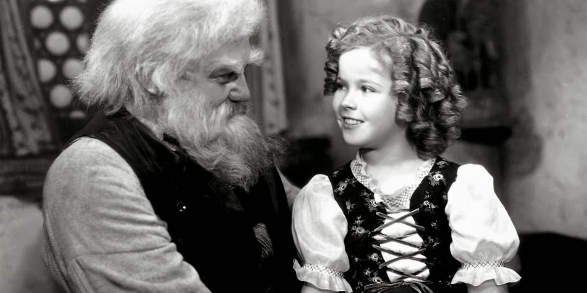 Shirley Temple sitting on Jean Hersholt's lap looking at each other in Heidi (1937)