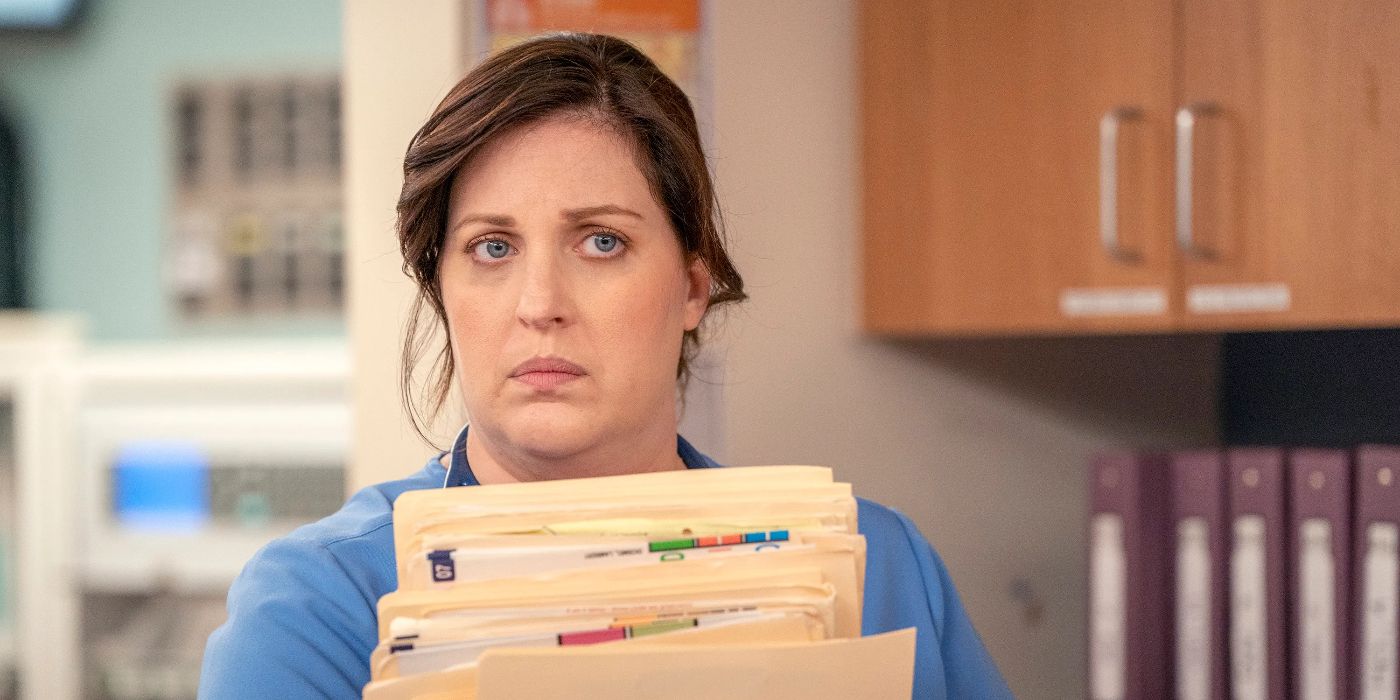 Alex (Allison Tolman) wearing blue nurse scrubs and holding a stack of medical folders while looking offscreen toward the right with a stern expression in St. Denis Medical