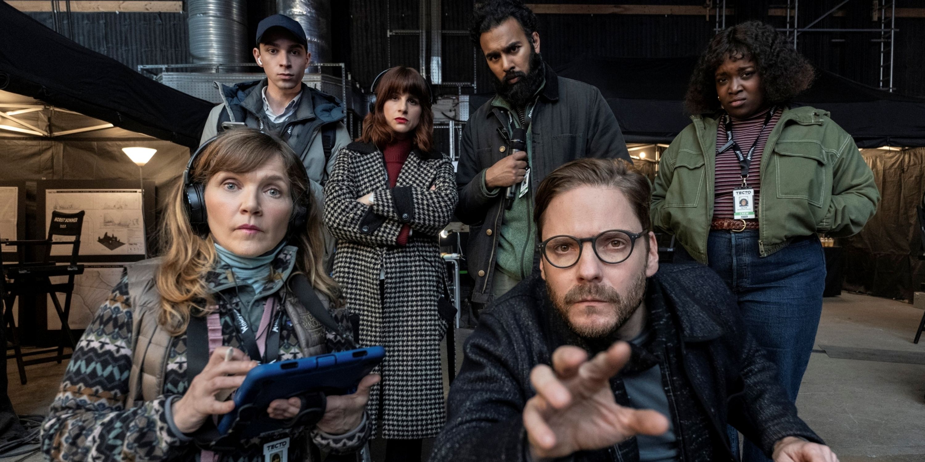 Daniel Brühl reaching with his right hand next to Jessica Hynes and other cast behind them in The Franchise