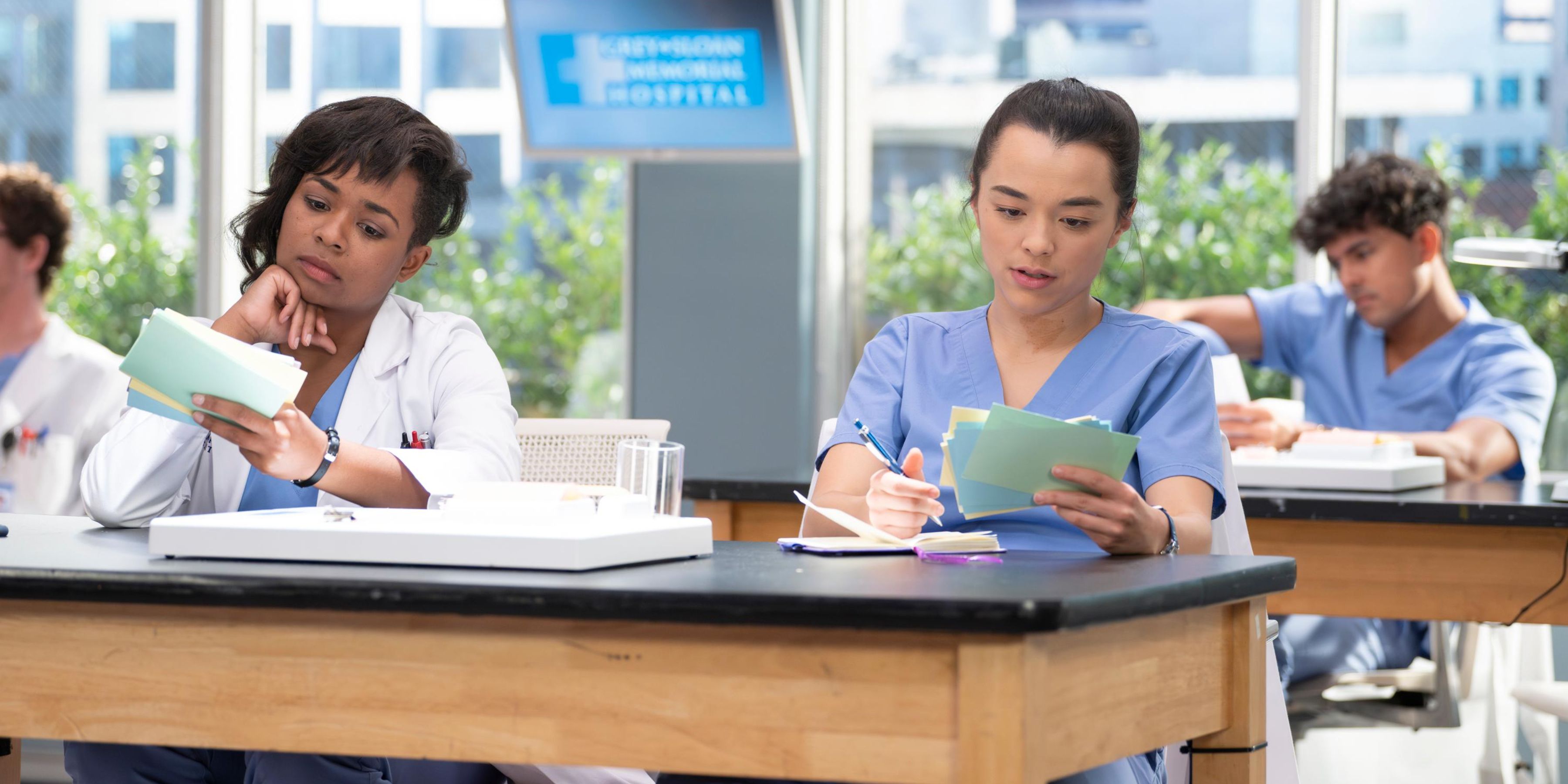 Alexis Floyd and Midori Francis as Simone and Mika in 'Grey's Anatomy' Season 20, sitting at a table looking at flash cards.