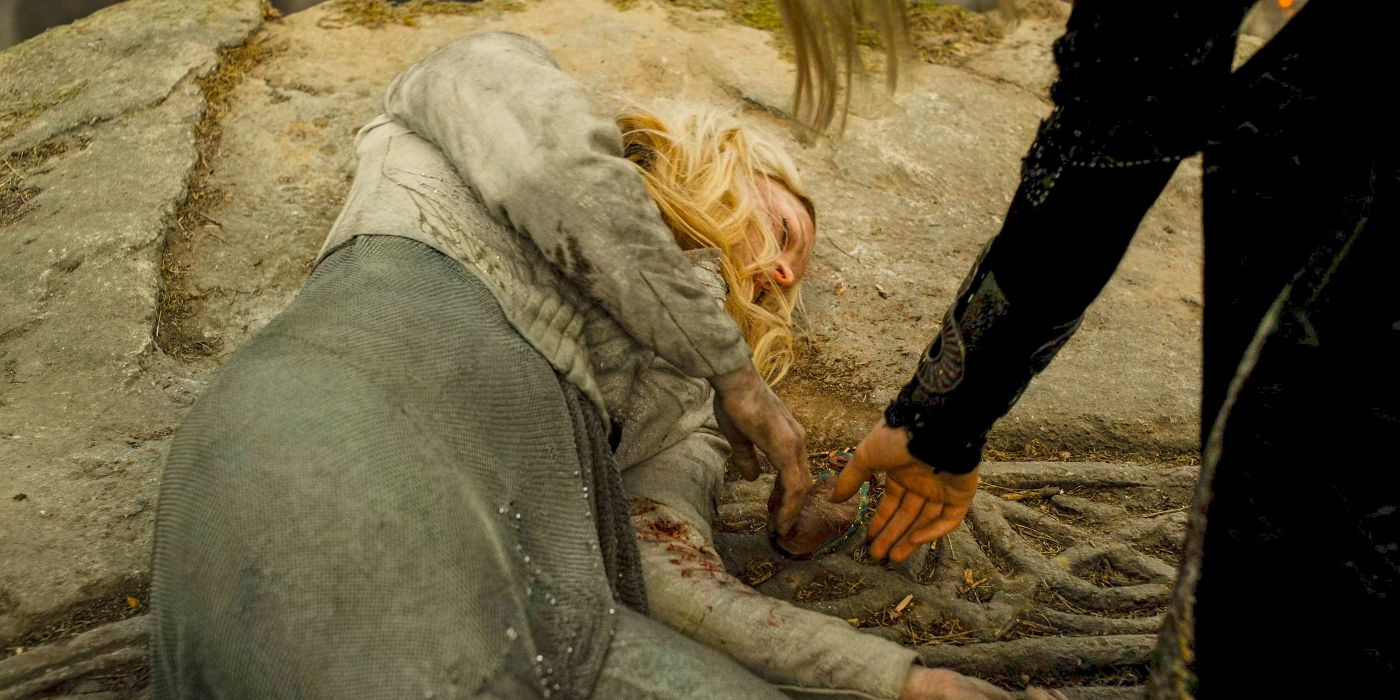 Galadriel (Morfydd Clark) lying injured on the ground as Sauron's (Charlie Vickers) hand reaches for a small bag on the ground near her body in The Rings of Power Season 2 finale