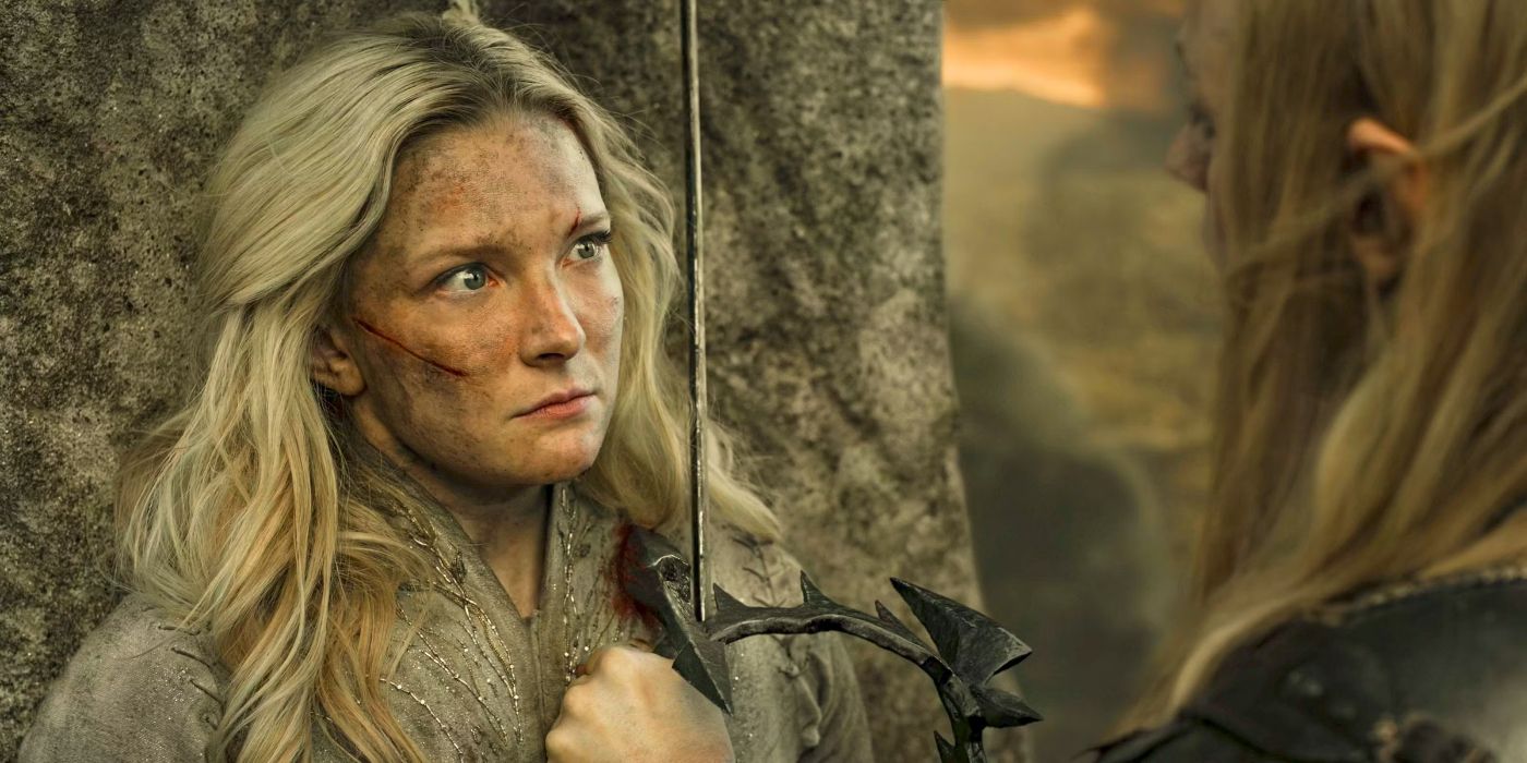 Galadriel (Morfydd Clark) staring at Sauron (Charlie Vickers) with an angry and hurt expression while he stabs her with Morgoth's crown and holds her against a tall stone in The Rings of Power Season 2 finale