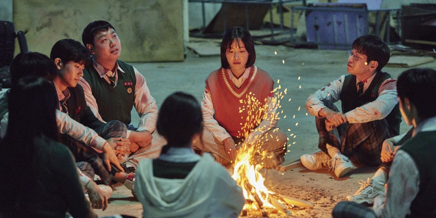 A group of private school students sit around a fire on a rooftop