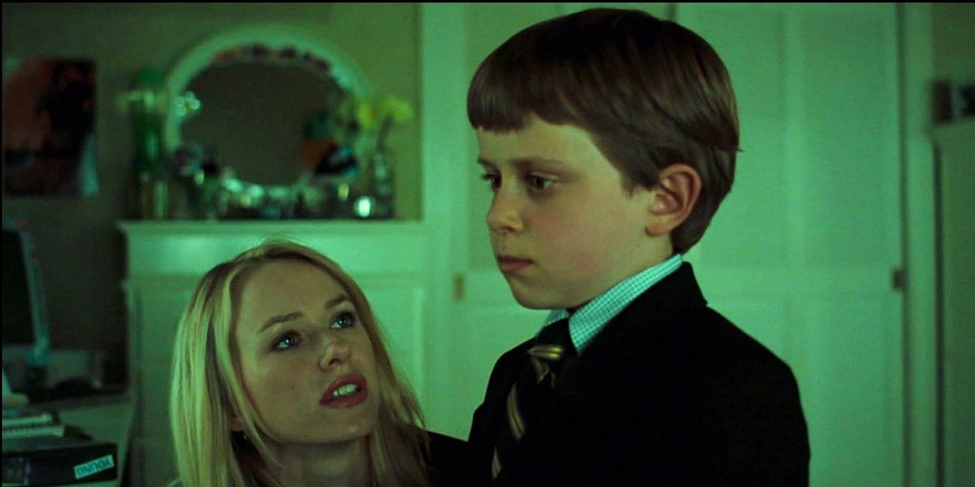 Naomi Watts as Rachel kneeling in front of her young son Aiden, played by actor David Dorfman, wearing a suit in &lsquo;The Ring&rsquo; (2002).
