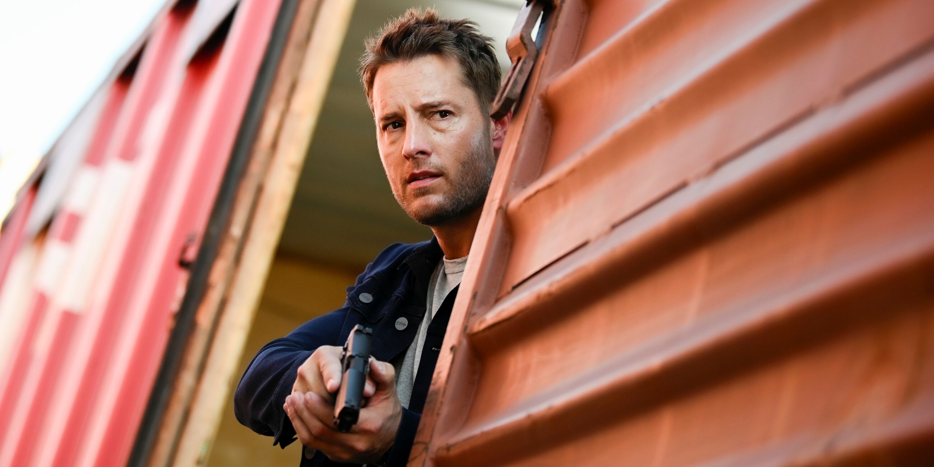 Justin Hartley as Colter Shaw holding a gun while looking out from a train car in Season 2 of Tracker