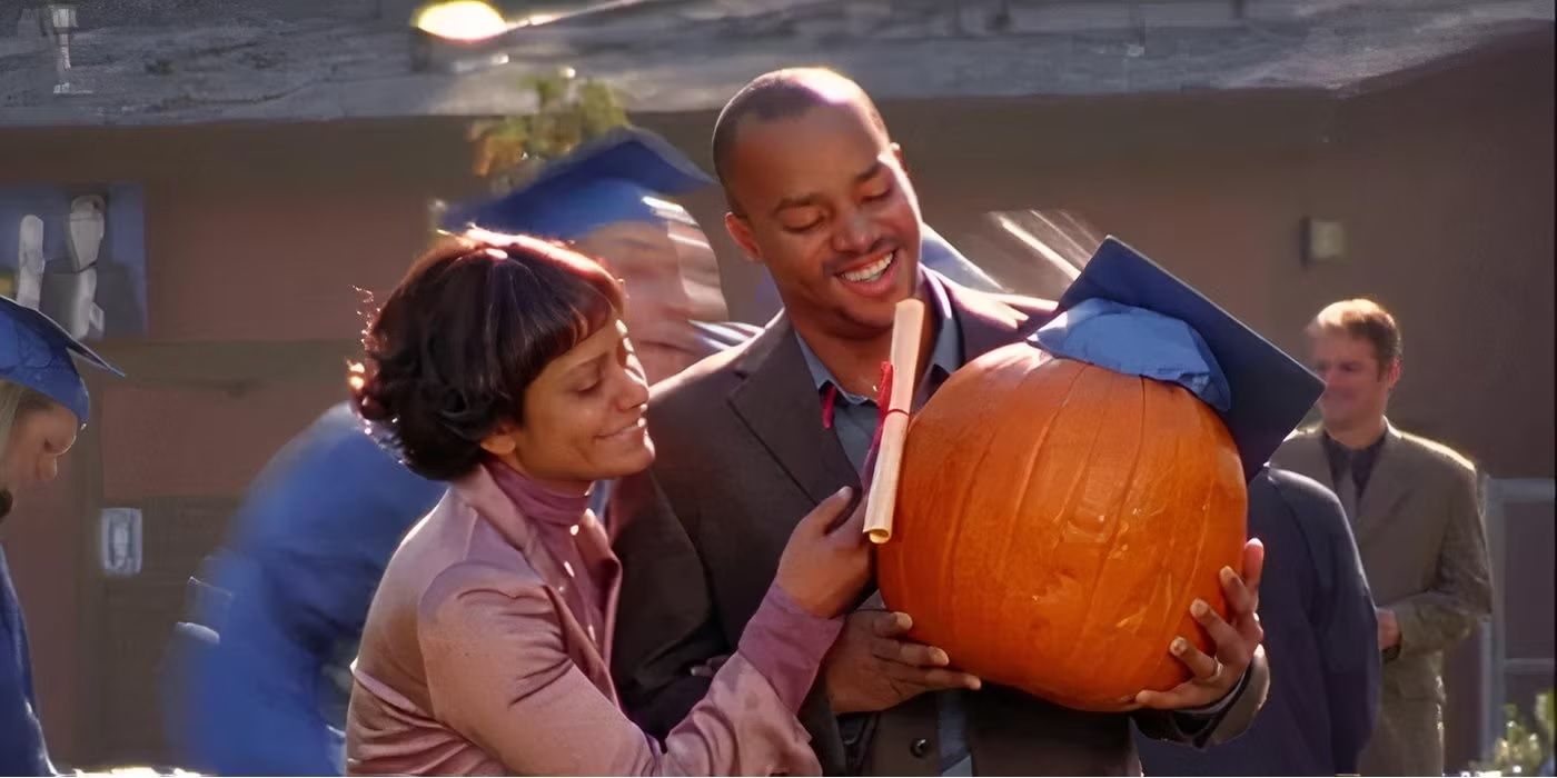 Turk and Carla holding a pumpkin with a graduation cap on and looking proud in Scrubs.